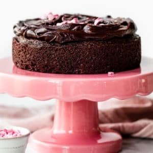 6 inch chocolate cake with chocolate ganache on top sitting on a pink cake stand.