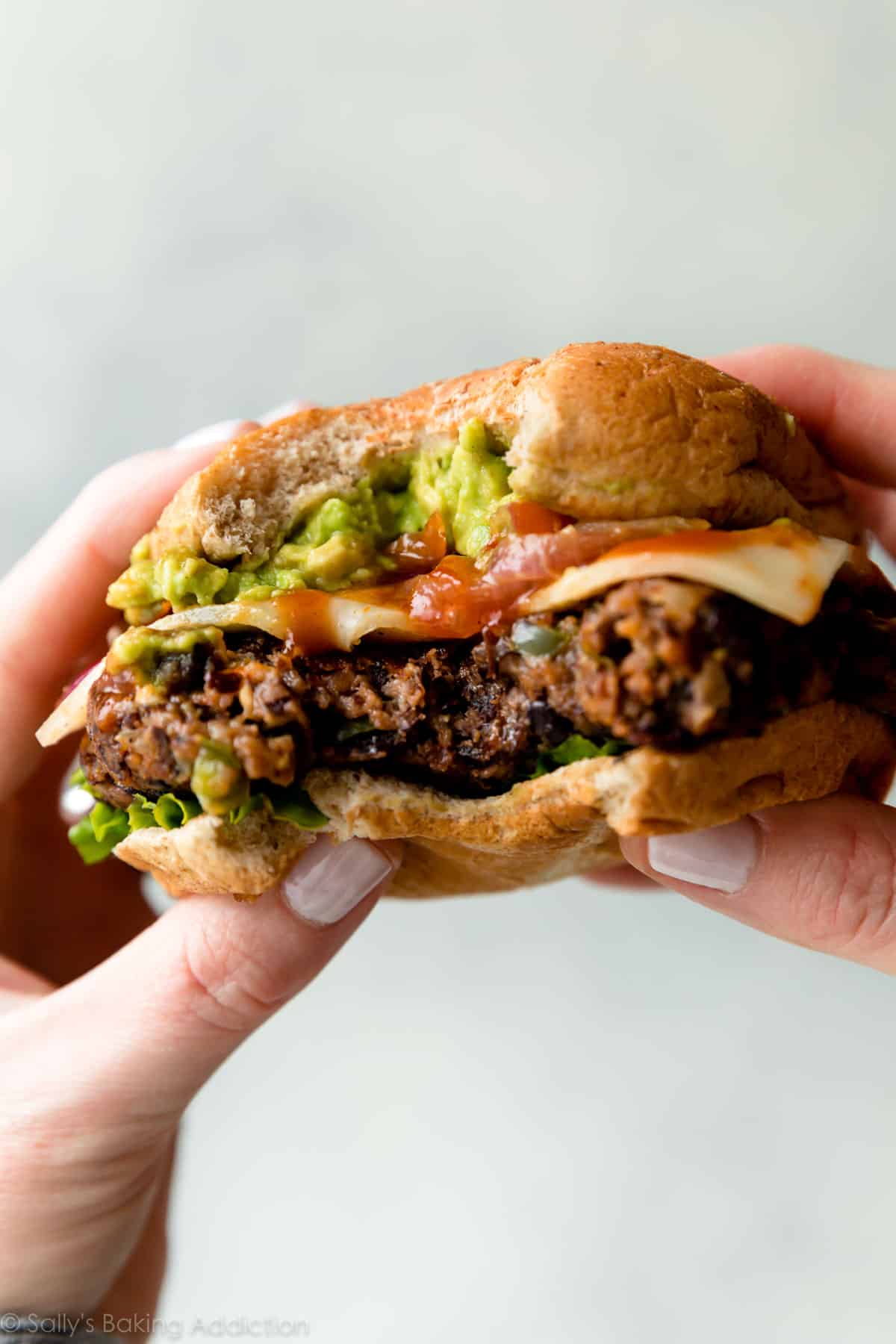 hands holding a black bean burger with a bite taken from it