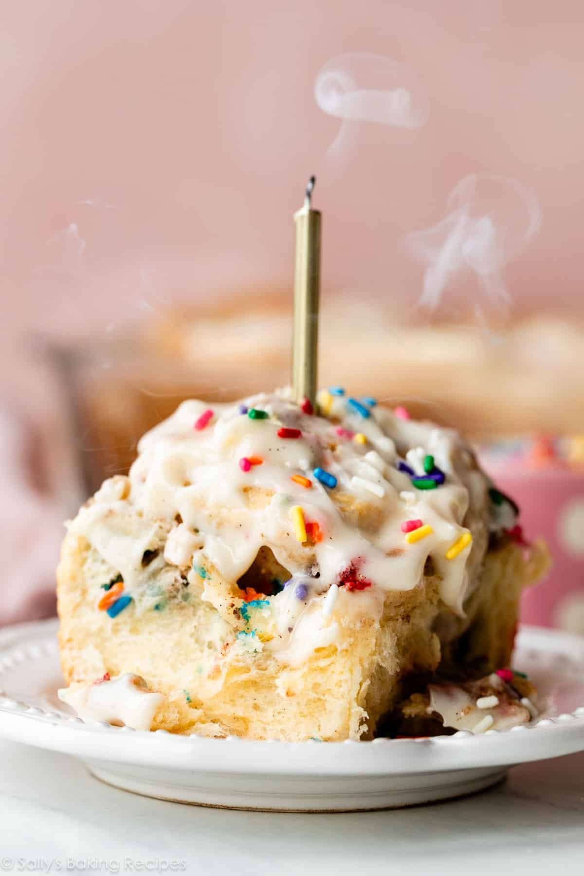 sprinkle funfetti cinnamon roll with cream cheese icing on top and a gold candle blown out.