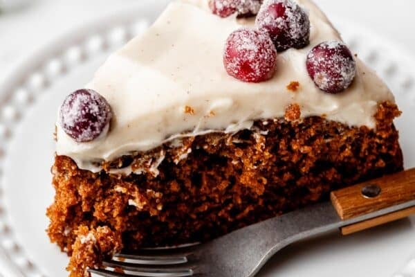 slice of gingerbread cake with cream cheese frosting on top and sugared cranberries.