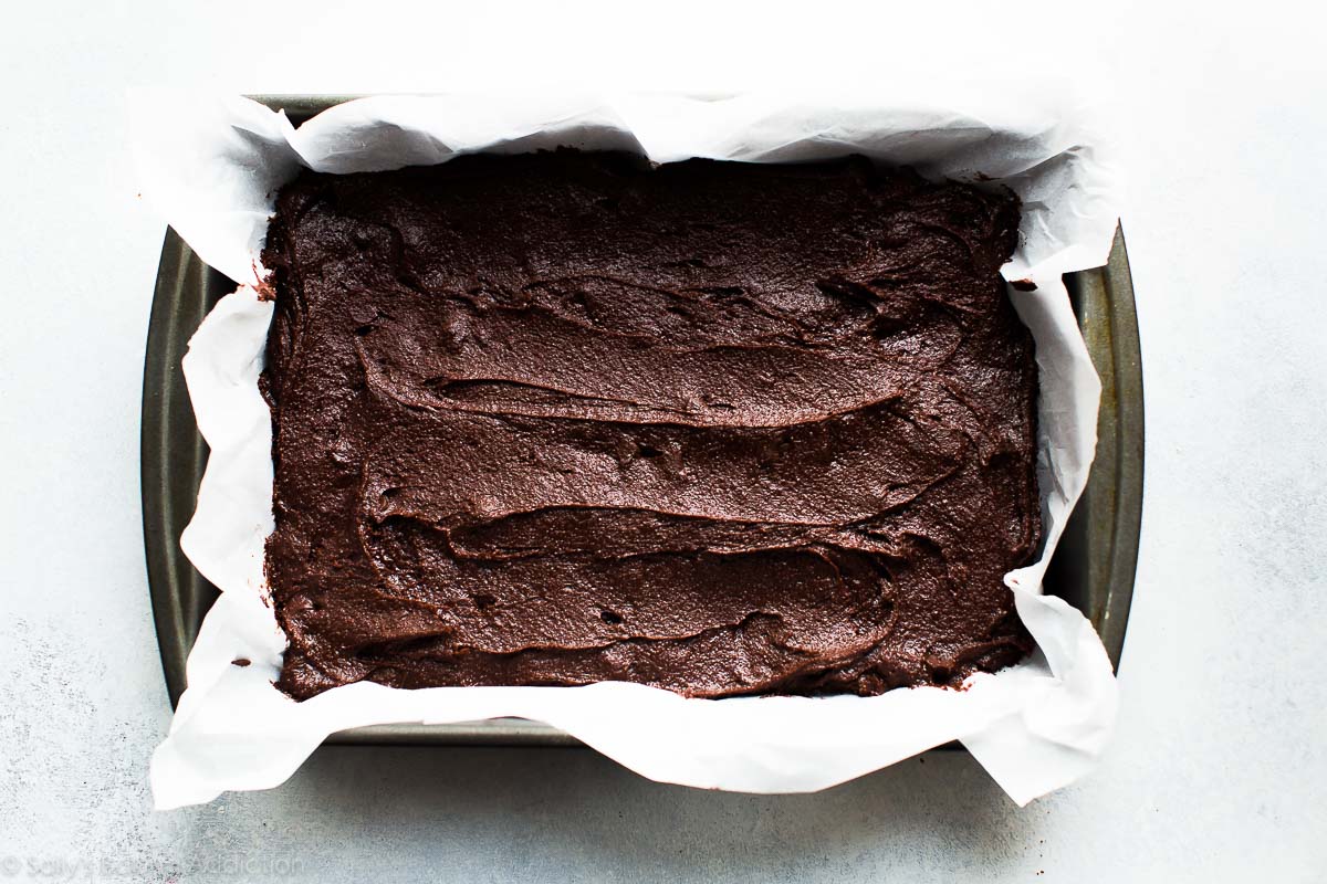 brownie batter spread into a baking pan lined with parchment paper