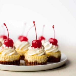mini cheesecakes with whipped cream and cherries on top on a white plate