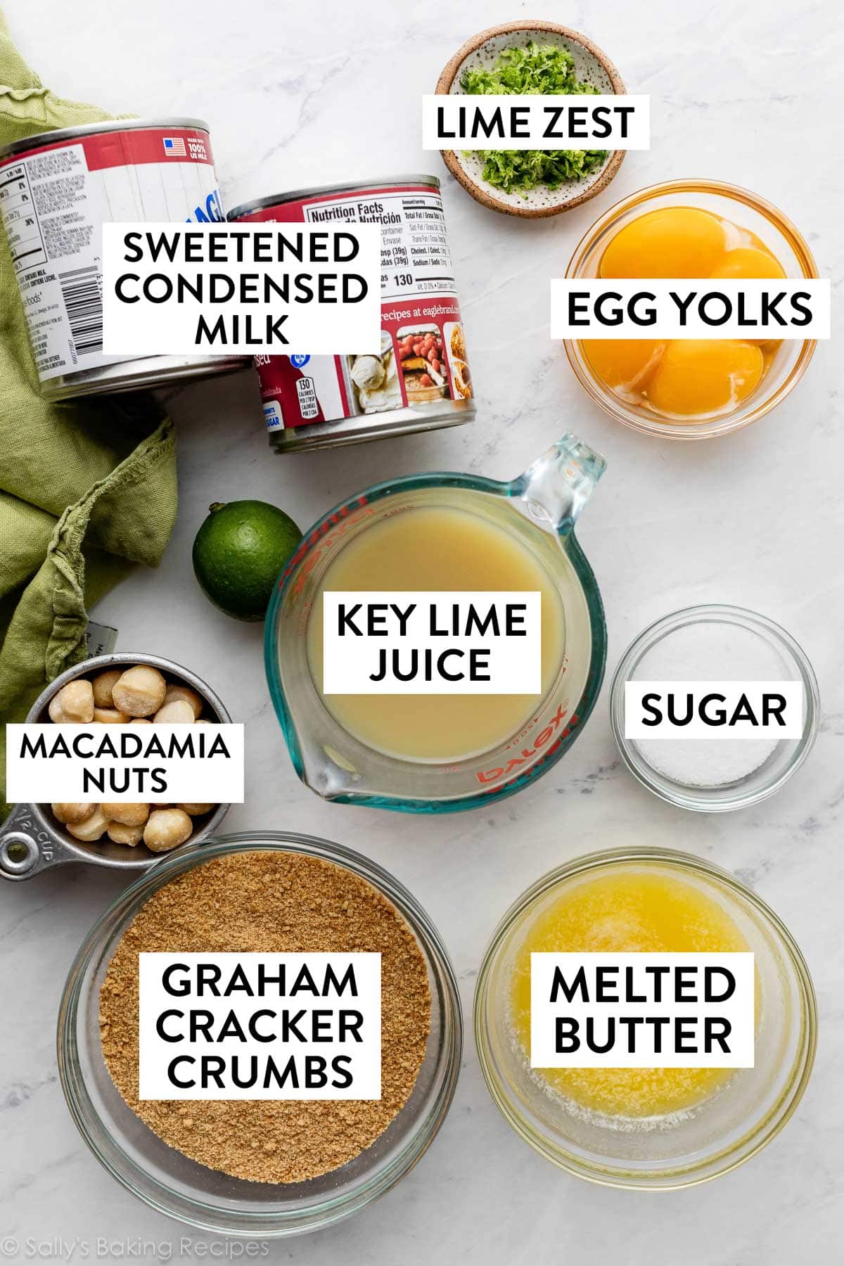 ingredients on counter including 2 sweetened condensed milk cans, egg yolks in bowl, melted butter, graham cracker crumbs, and sugar.