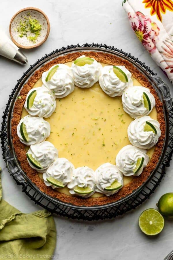key lime pie with whipped cream piped on top in a graham cracker crust on a round wire cooling rack.