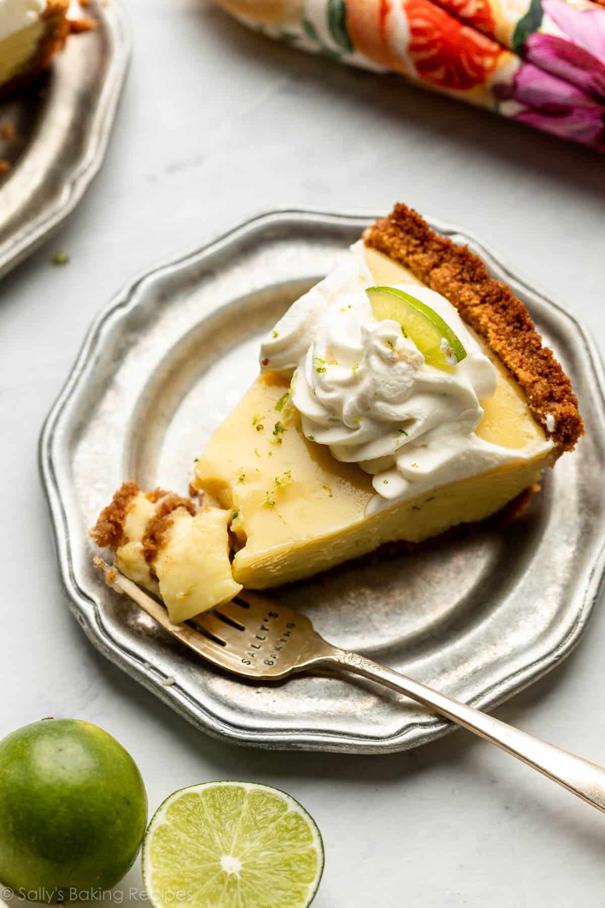 key lime pie slice on silver plate with whipped cream on top.