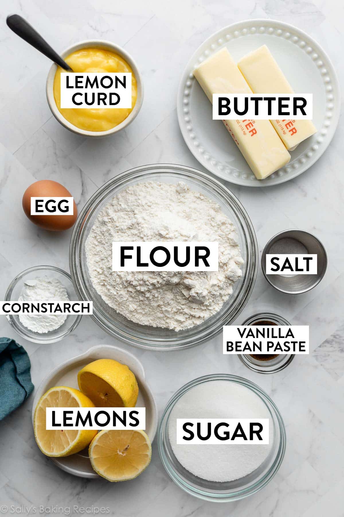 ingredients on marble counter including flour, butter, salt, lemons, lemon curd, sugar, and cornstarch.
