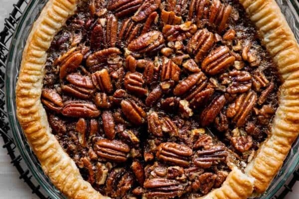 pecan pie in glass pie dish with slice already cut and about to be taken out with pie server.