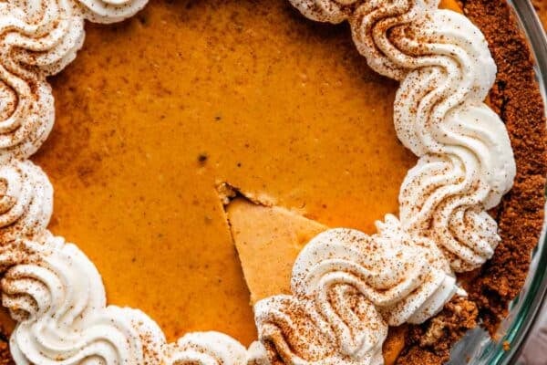 pumpkin cheesecake pie with whipped cream on top and slice being taken out.