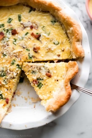 Quiche with bacon in a white pie dish with a slice being removed