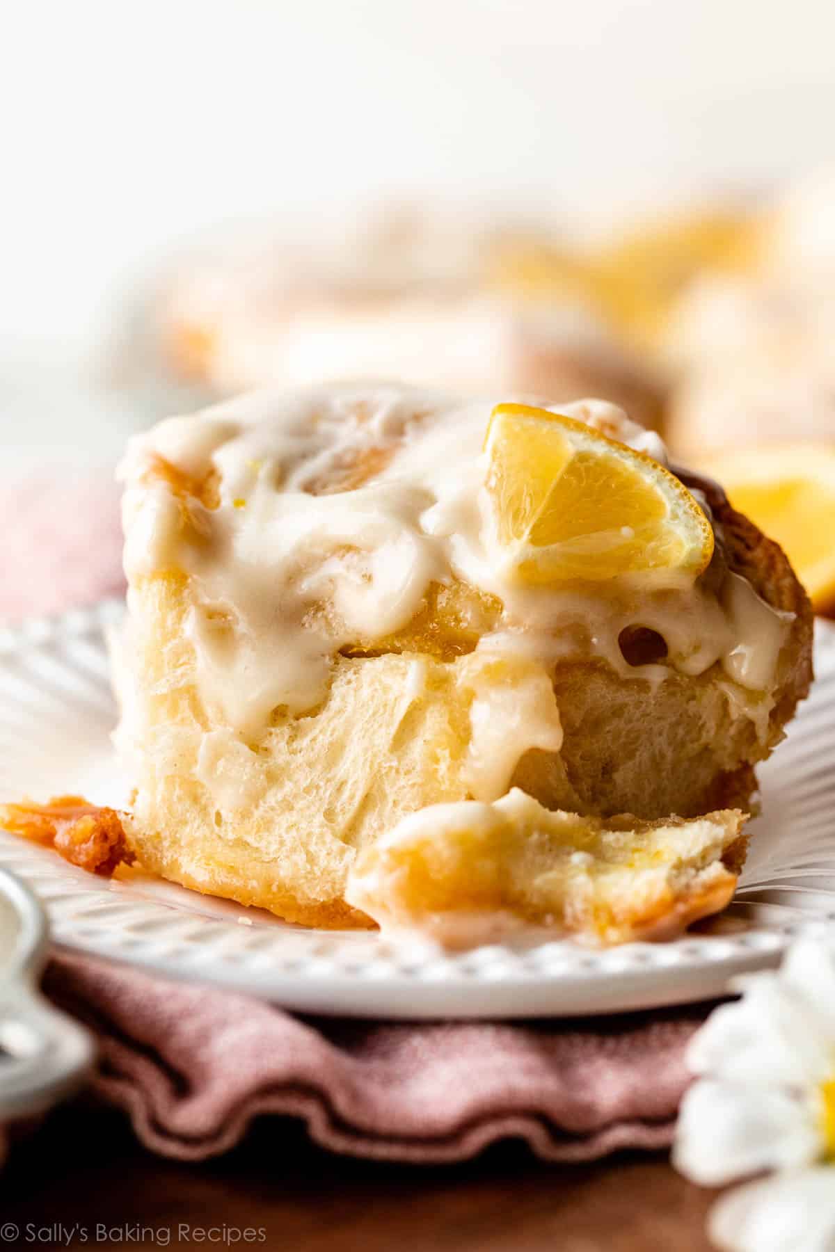 close-up of lemon sweet roll with lemon slice on top on a white plate.
